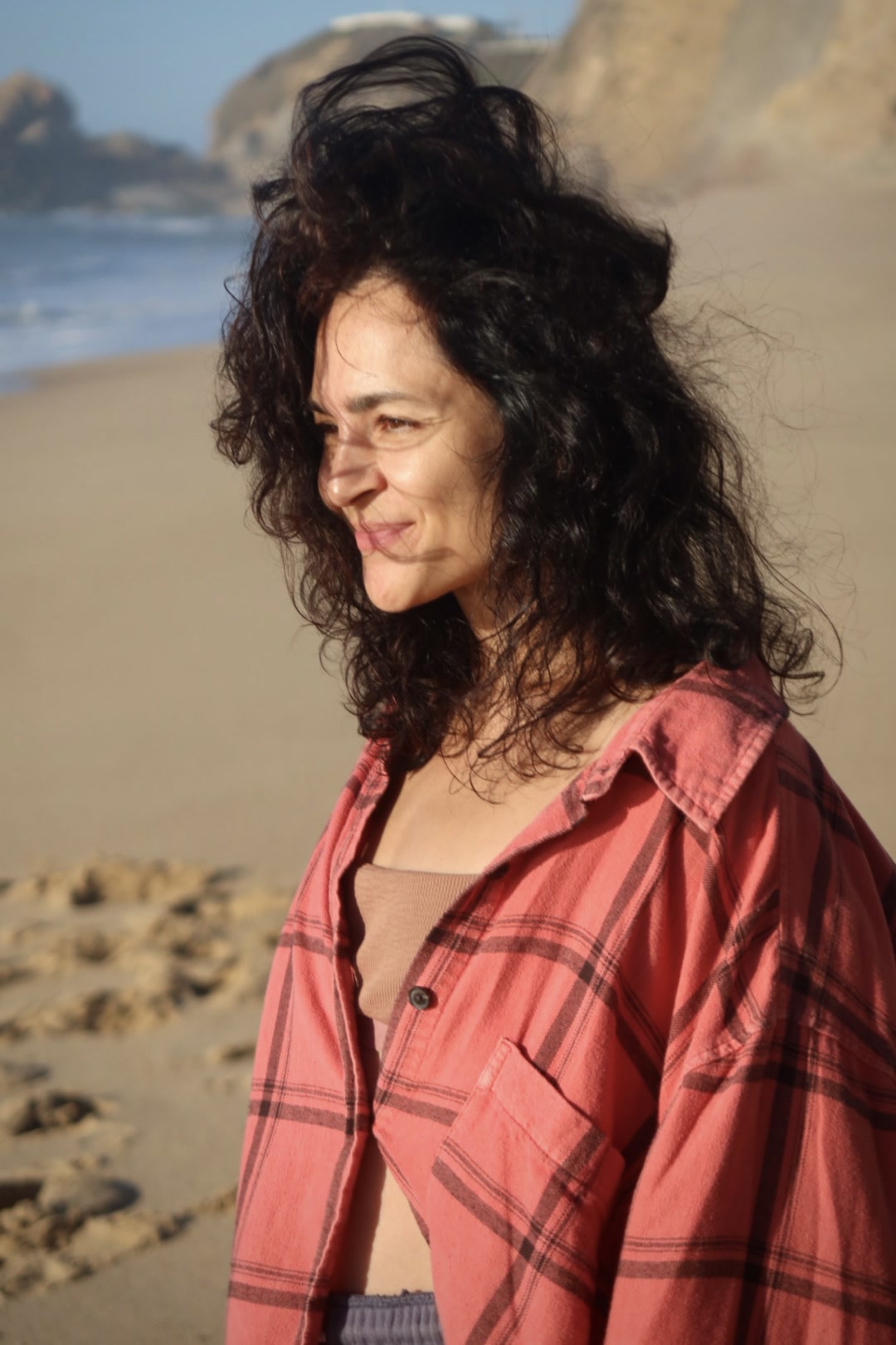 Karina, author of Marathon 4.0, smiling on the beach, wind in her curly hair
